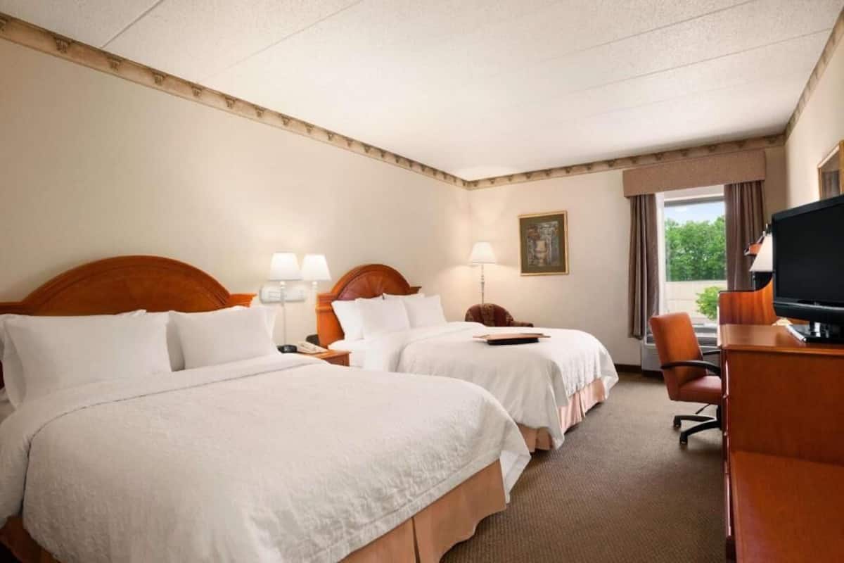 A hotel room with two beds, a desk, a chair, a television, and a window with curtains.