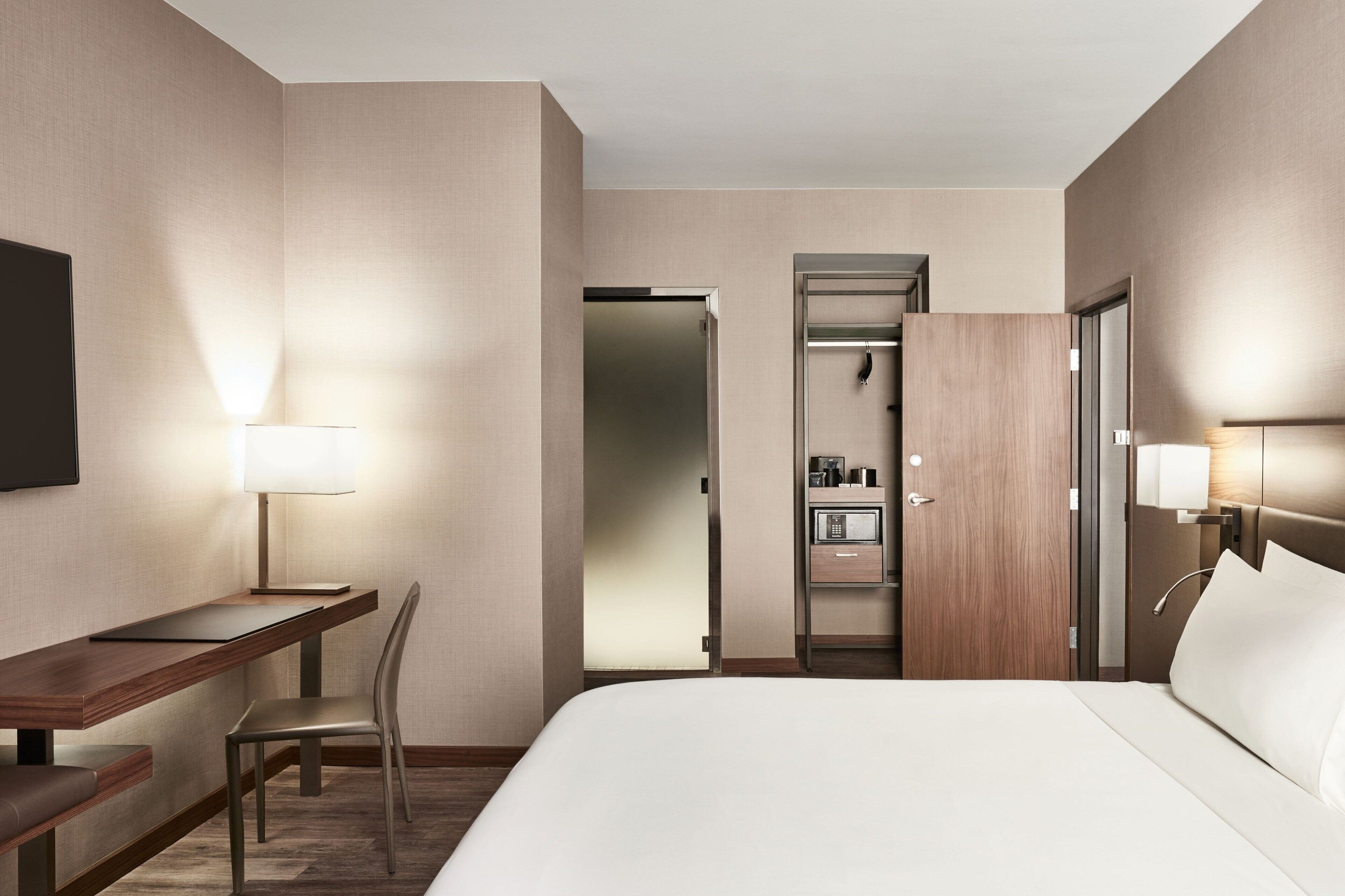Ein Hotelzimmer mit Bett, Schreibtisch, Stuhl und einem begehbaren Kleiderschrank mit Mikrowelle.