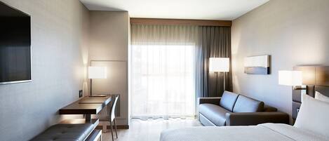 Una habitación de hotel moderna con una cama grande, un escritorio con silla, un sofá y un televisor montado en la pared.