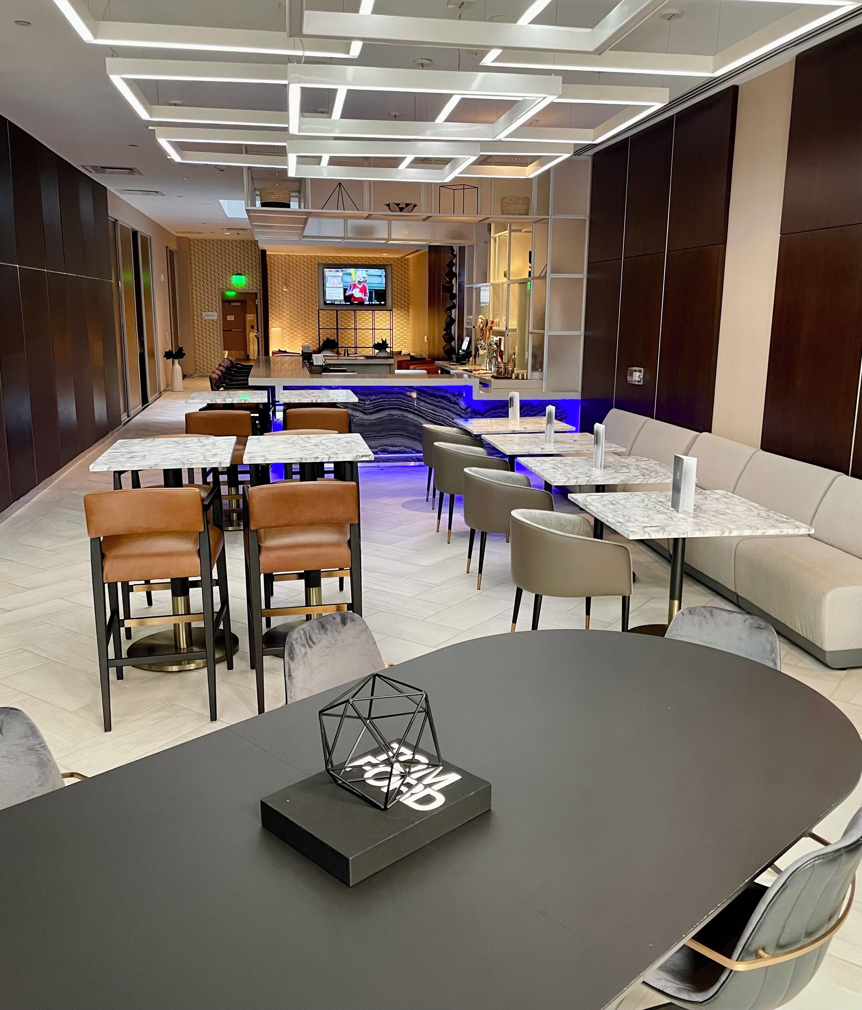 A modern hotel lobby with a reception area, seating arrangements, and a TV screen.