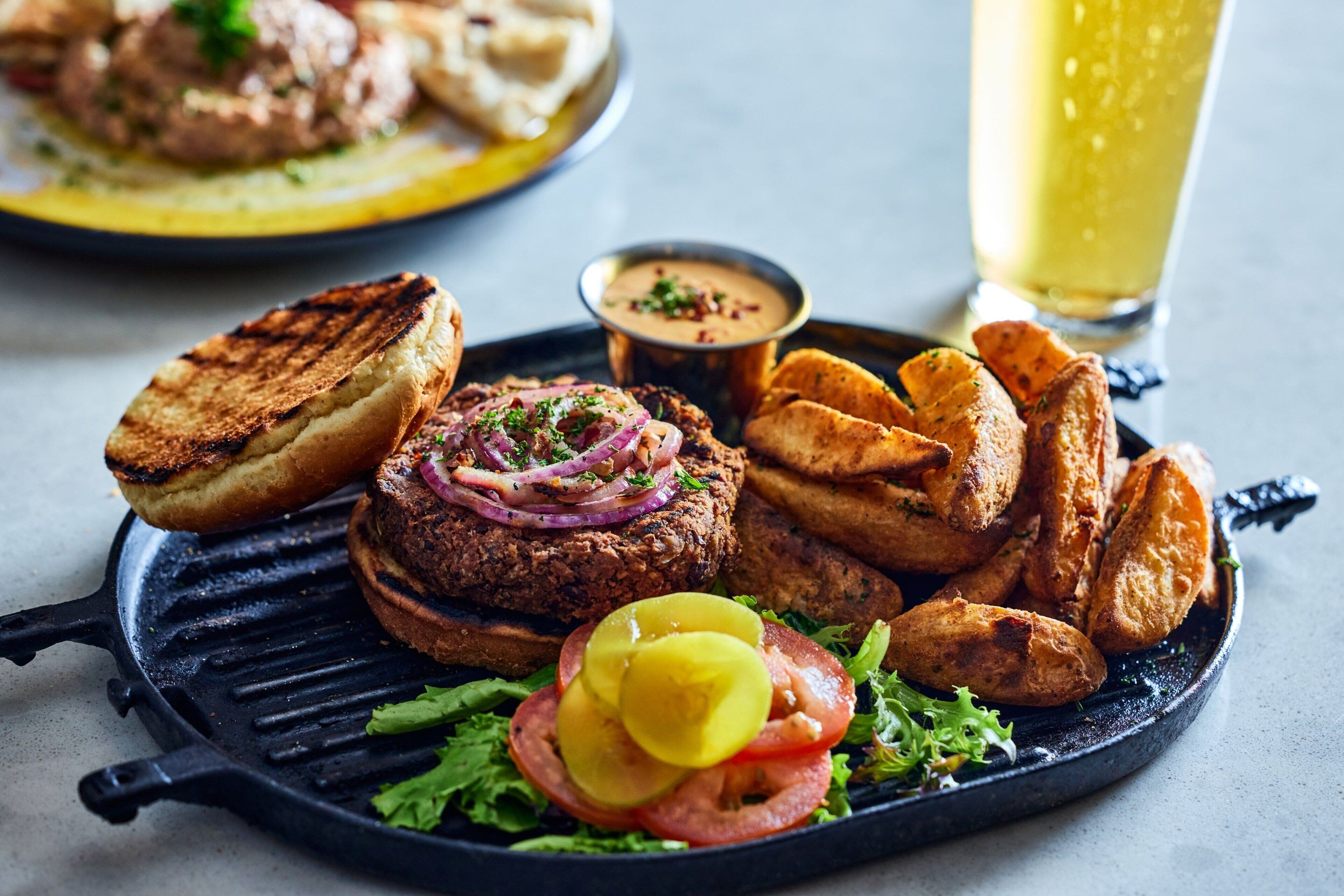 A meal with grilled patties, potato wedges, and a side salad on a cast iron skillet.