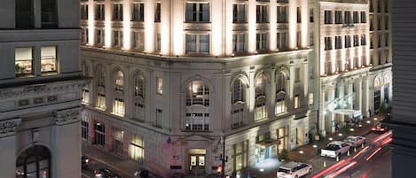 A historic building with classical architecture, a prominent corner entrance, and a street with light trails indicating traffic.