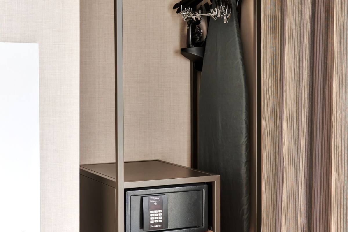 A compact room with a bunk bed, a small desk with a SmartBox device, and a coat rack with a hanging garment.