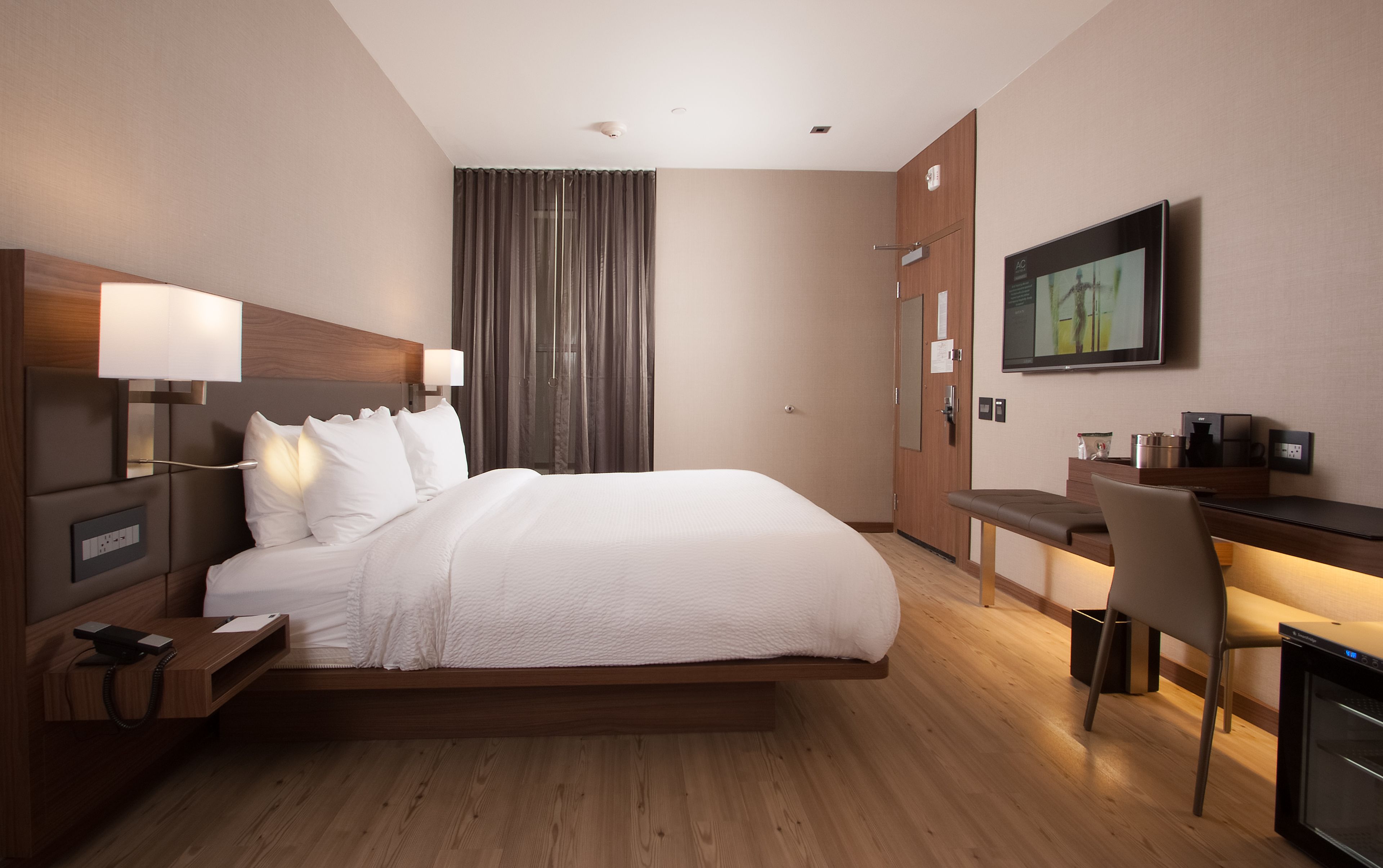 A hotel room with a bed, bedside table, lamp, desk, chair, and TV.