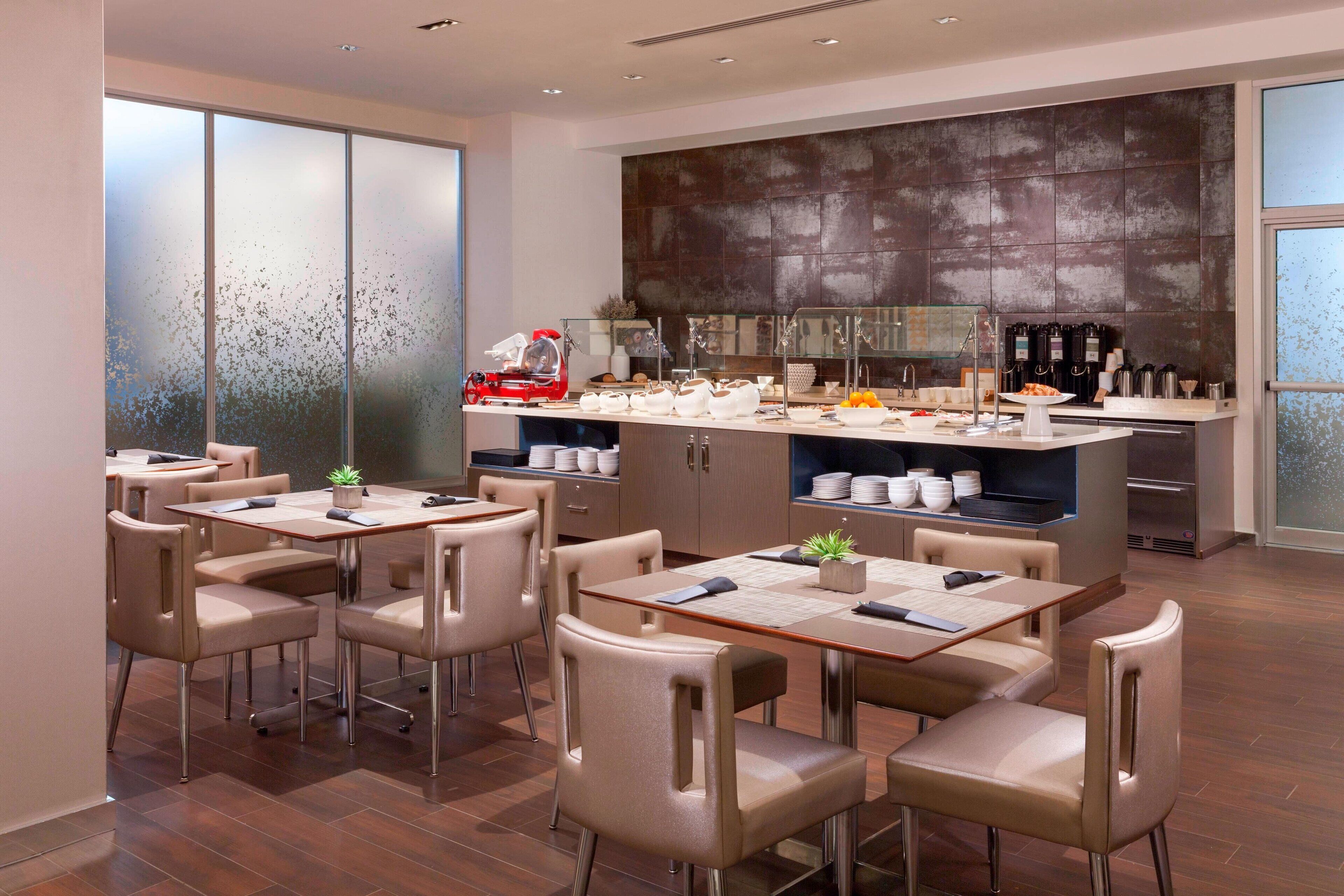 A modern kitchen with a central island, a dining area with chairs, and a large window.