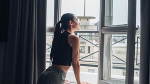 Una persona apoyada en el alféizar de una ventana, con vistas a edificios.