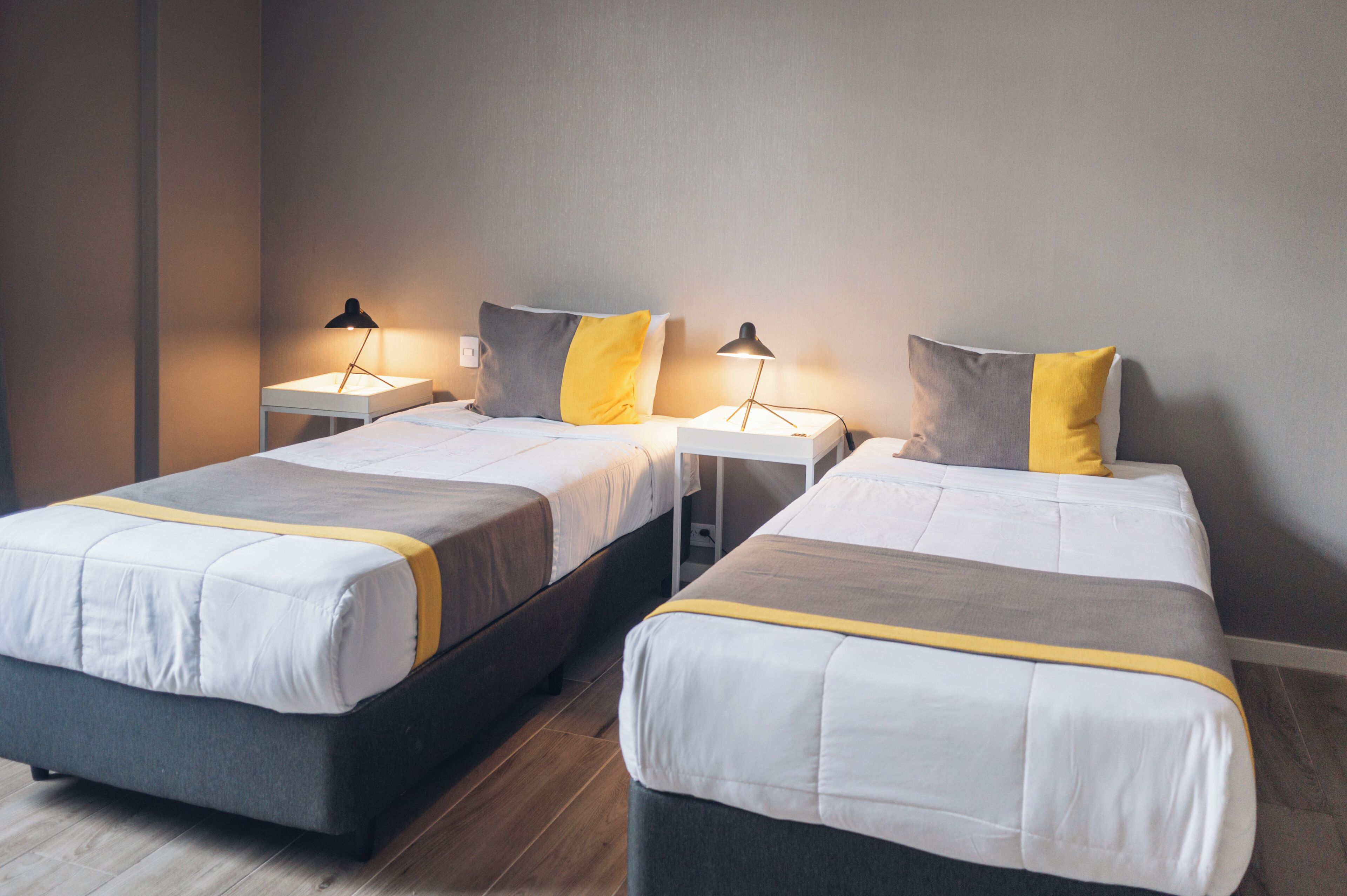 A hotel room with two beds, each with a bedside table and lamp, and a neutral color scheme.