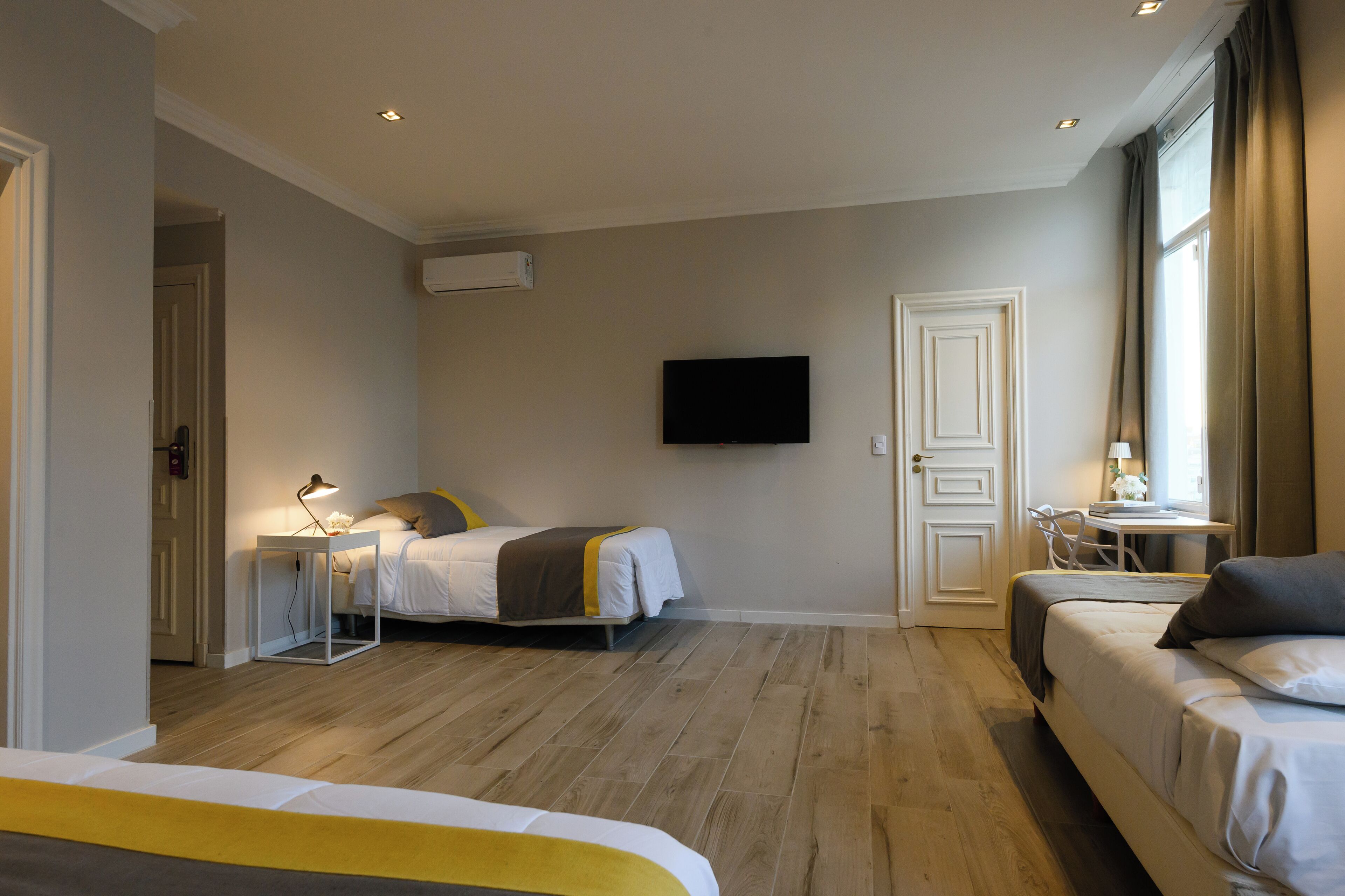 Quarto de hotel com duas camas, uma escrivaninha, uma cadeira, uma TV e uma janela.