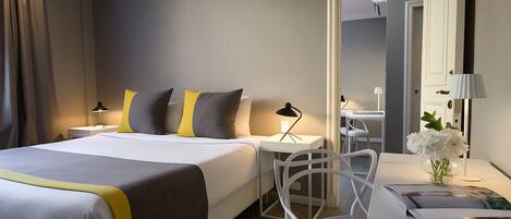 A modern hotel room with a bed, bedside tables, a desk, and a chair.