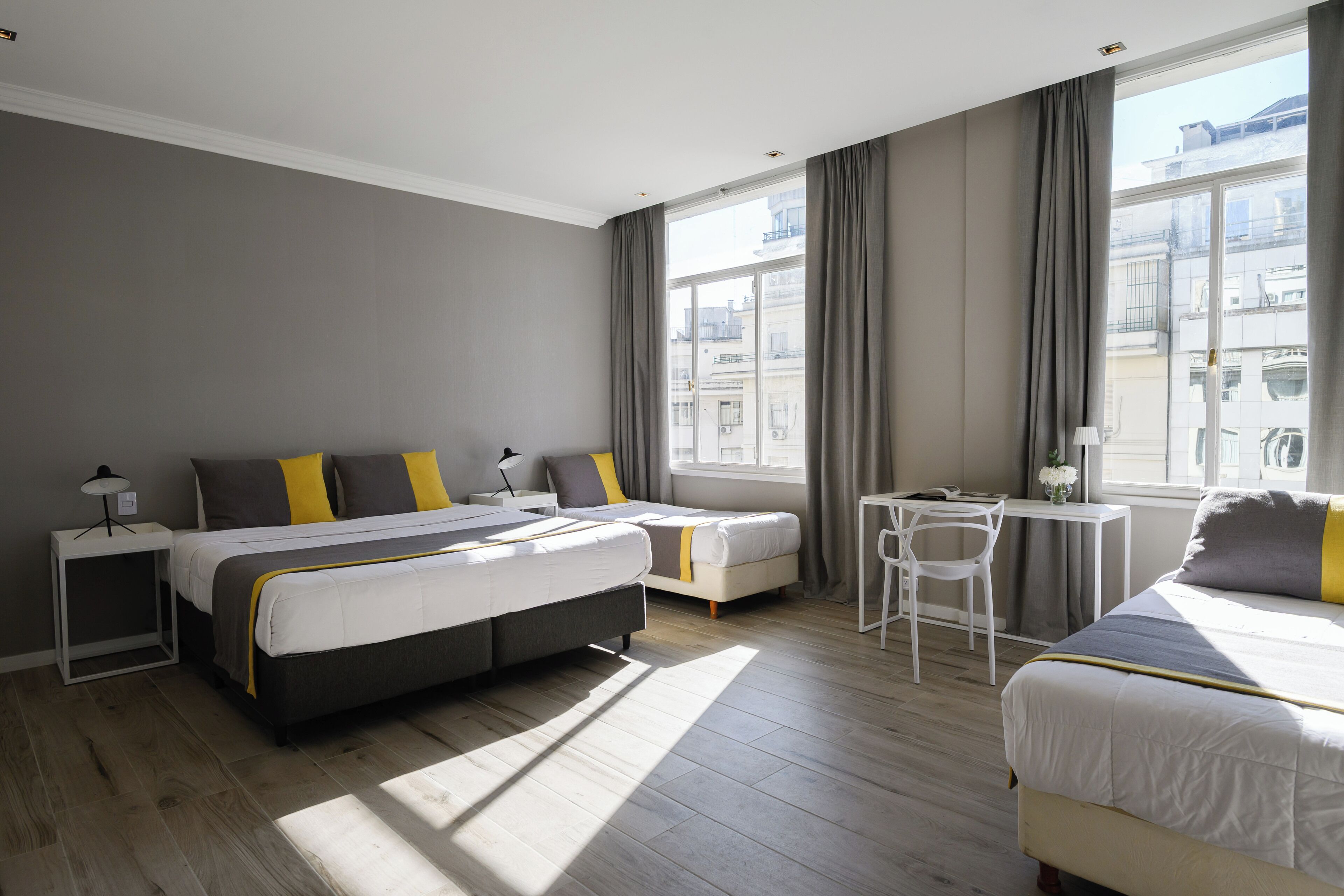 Ein modernes Hotelzimmer mit einem großen Bett, einem kleineren Bett, einem Schreibtisch und einem Stuhl.