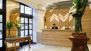 A reception desk with a wooden finish and a modern design, a bench with a glass top, and a large vase with flowers. - Midtown Boutique Hotel (Buenos Aires)