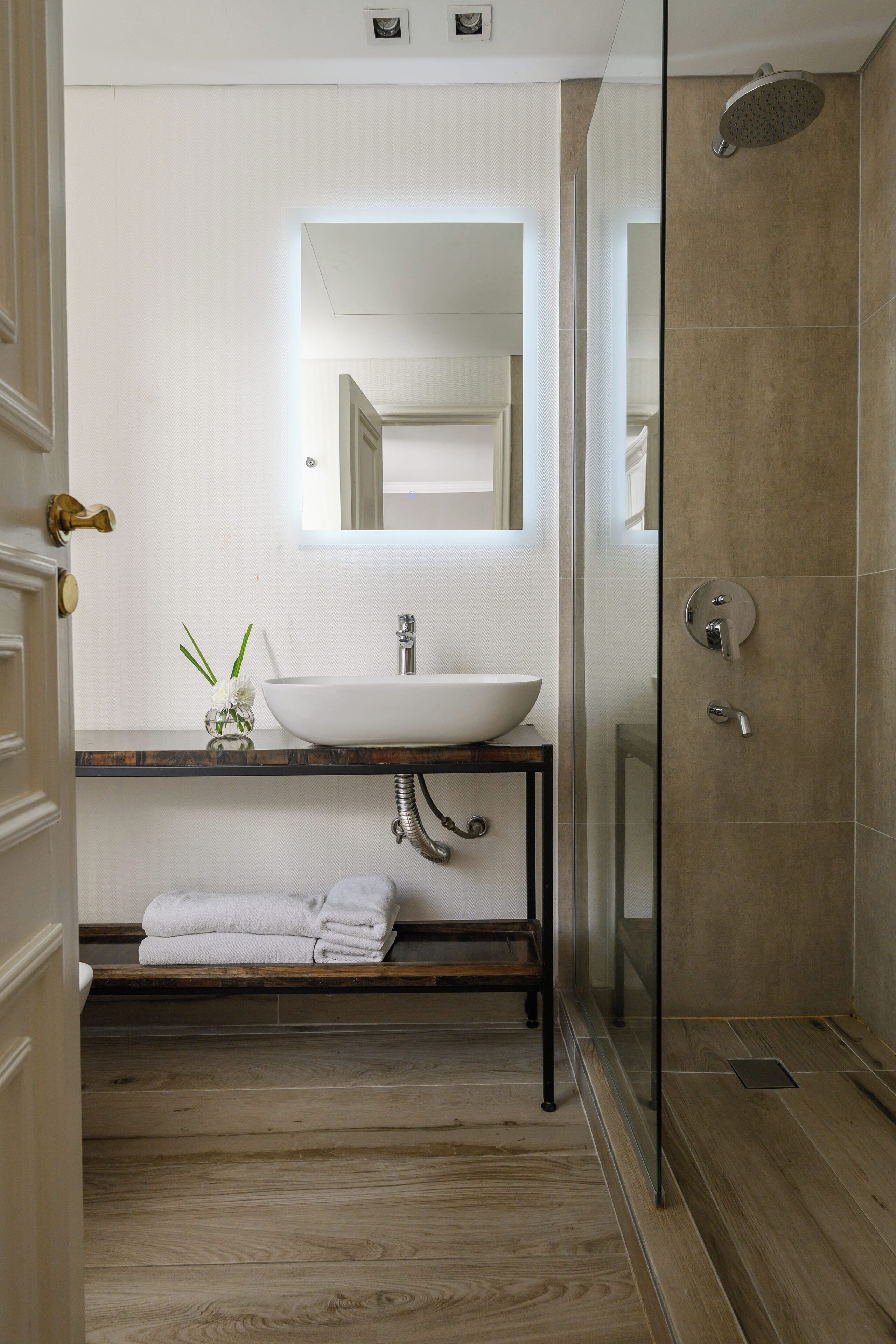 Un baño moderno con un lavamanos blanco, una cabina de ducha de vidrio y piso de madera.
