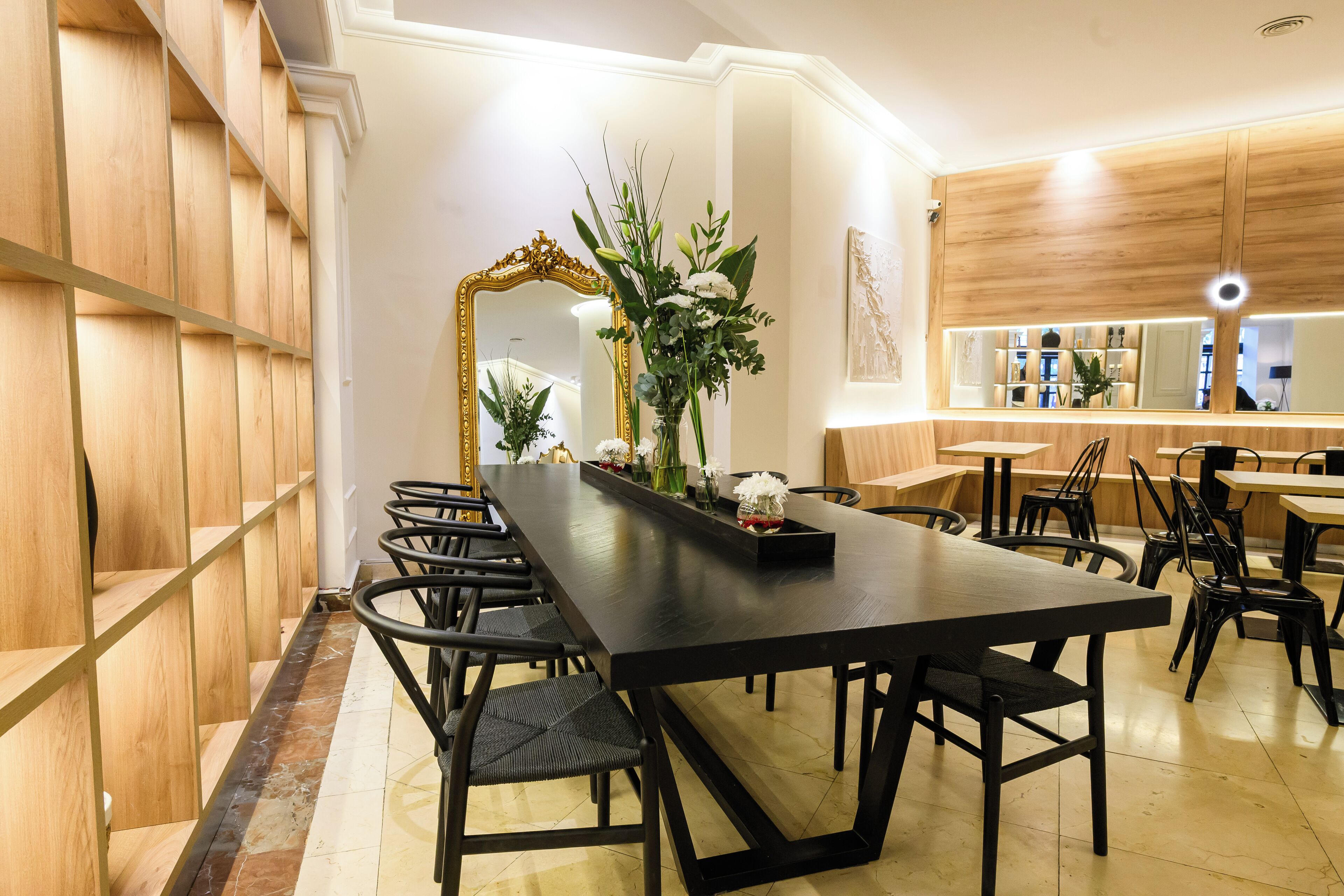 A modern dining area with a long table, black chairs, and a decorative floral arrangement.