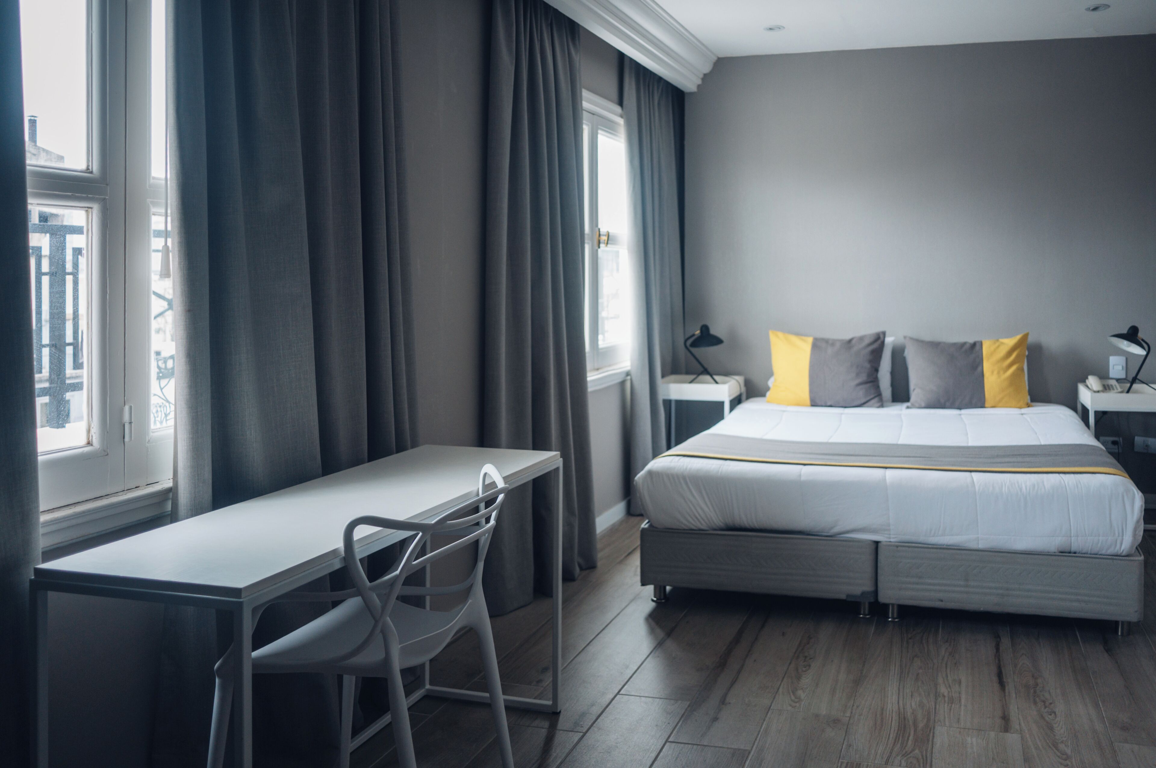 A modern hotel room with a bed, desk, chair, and curtains.