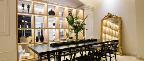 A dining area with a long table and six chairs, a mirror with an ornate frame, and a built-in shelving unit with various decorative items.