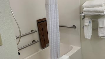 A bathroom with a bathtub, a shower curtain, a towel rack with towels, and a wooden door.