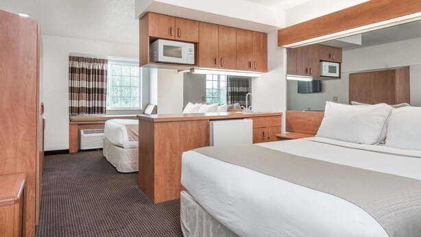 A modern hotel room with a large bed, wooden cabinets, a microwave, and a desk with a chair. - Microtel Inn & Suites by Wyndham Rice Lake (Rice Lake)