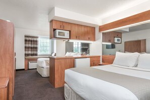 A modern hotel room with a large bed, wooden cabinets, a microwave, and a desk with a chair.