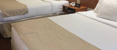 A hotel room with two beds, a bedside table with a phone, and a mirror above the headboard.