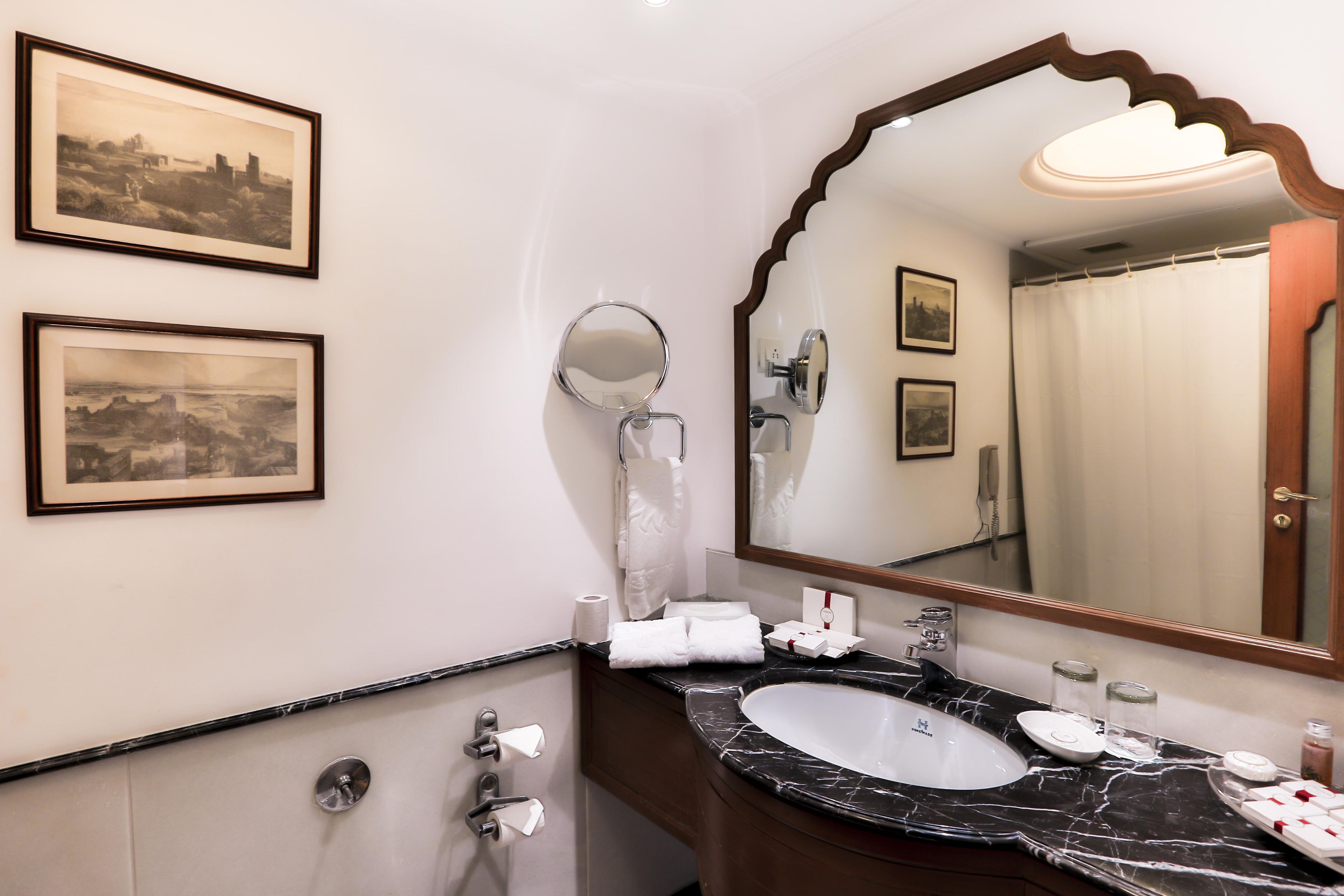 A bathroom with a marble sink, a large mirror, framed pictures on the wall, and a shower curtain.