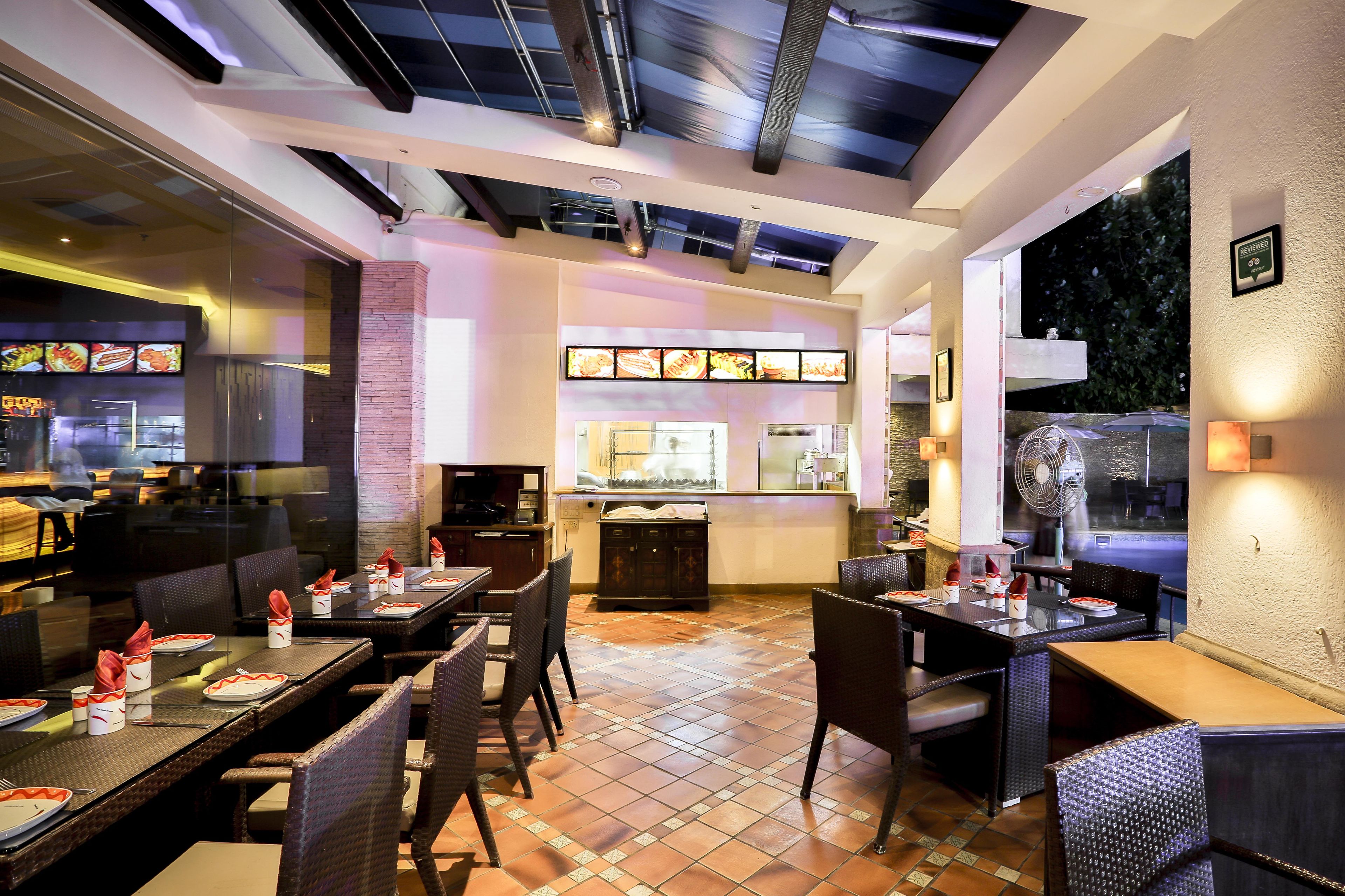 Un restaurante con varias mesas, sillas y una cocina visible a través de un separador de vidrio.