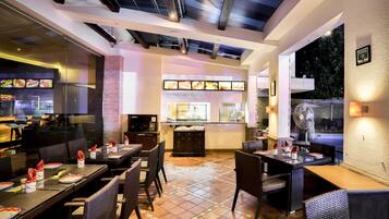 Un restaurante con varias mesas, sillas y una cocina visible a través de un separador de vidrio.