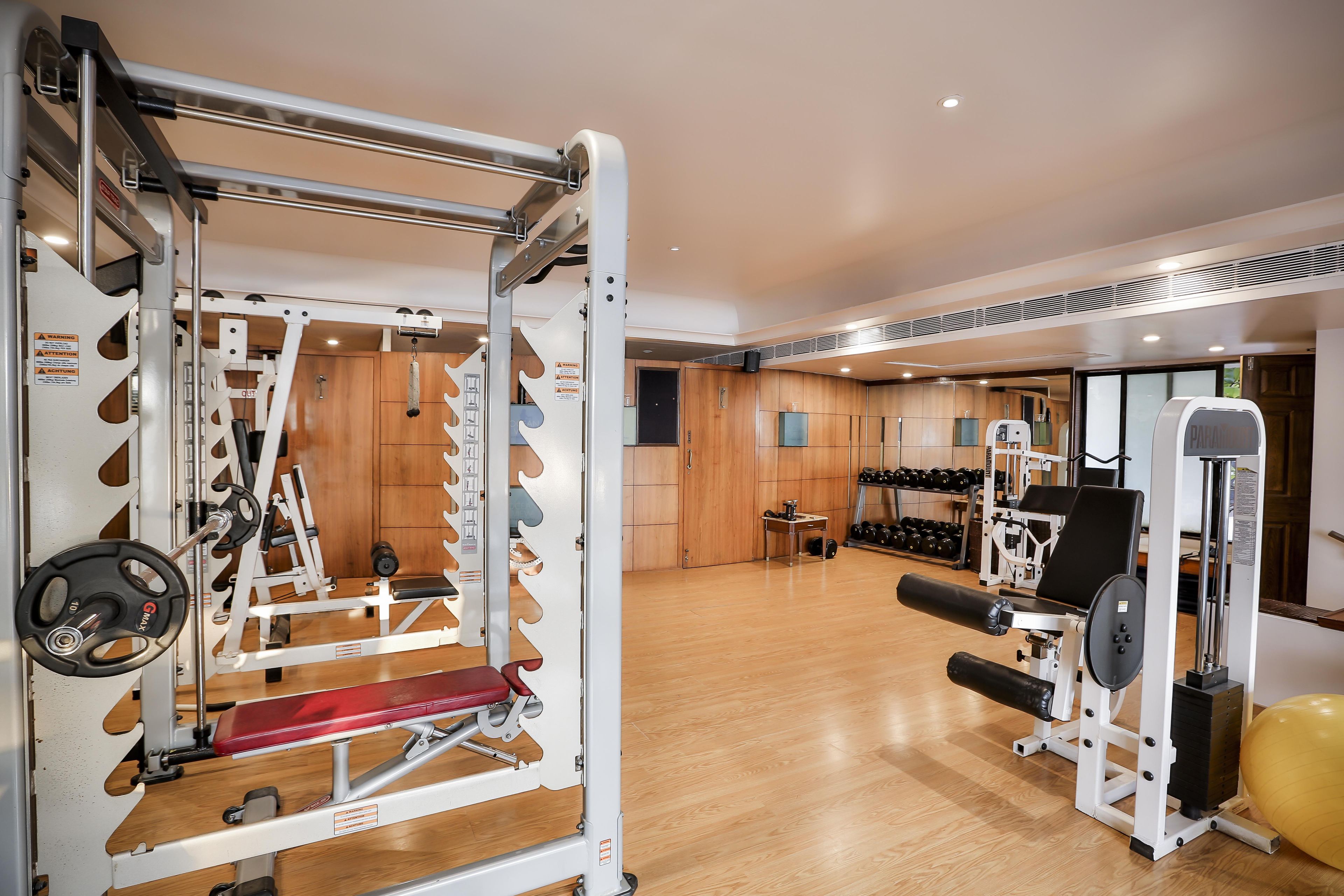 Un gimnasio con equipamiento de levantamiento de pesas, suelo de madera y un muro espejado.