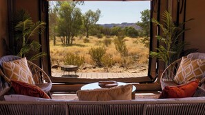 A room with a view of a desert landscape, featuring a wicker sofa with patterned cushions and a small round table. - Discovery Resorts - Kings Canyon (Petermann)