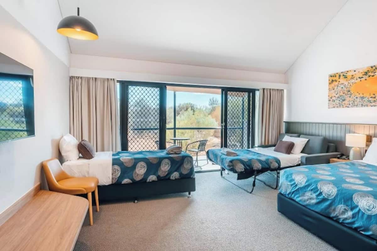 A hotel room with two beds, a desk, a chair, and a balcony with a view.