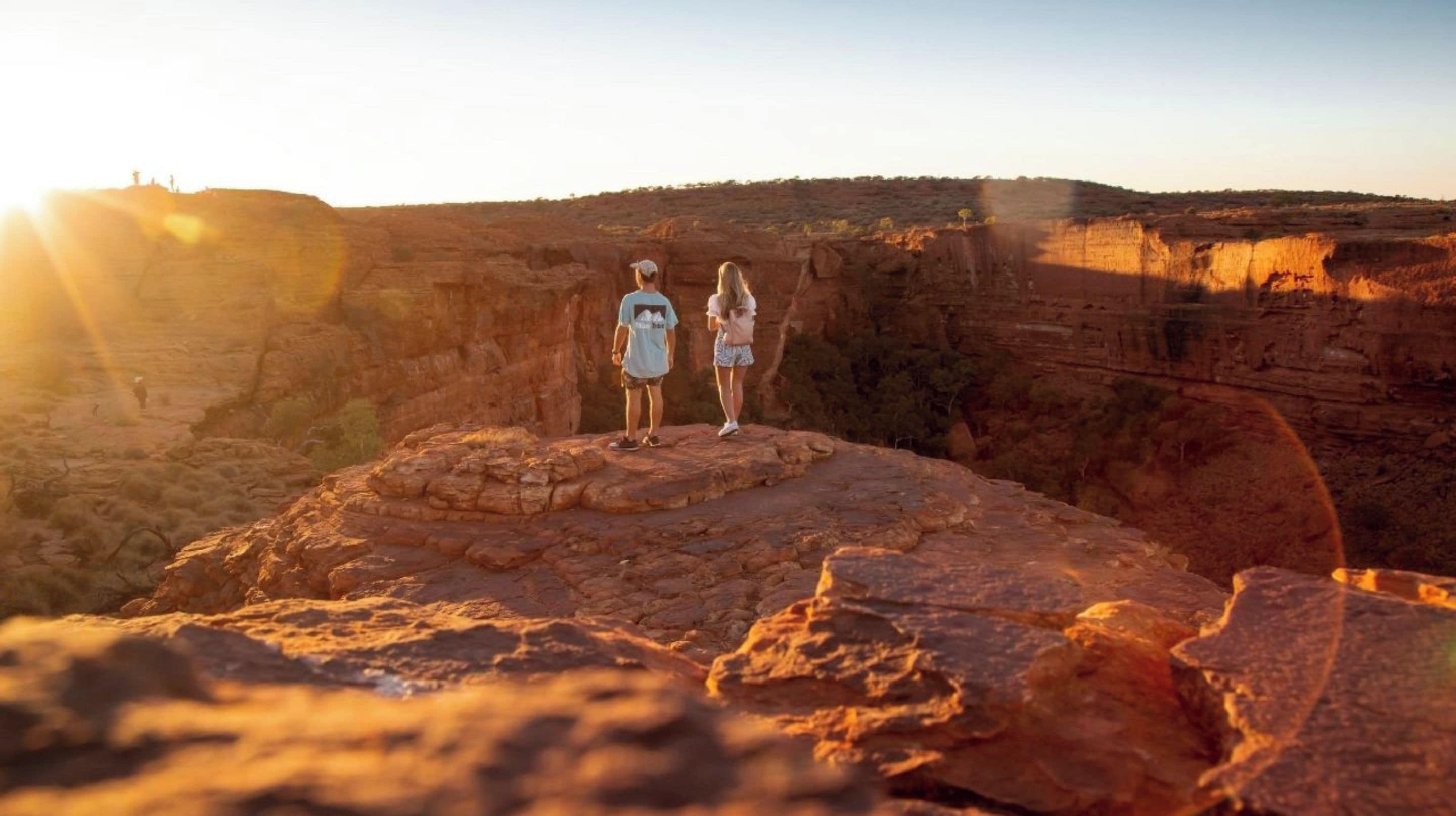 Two people standing on a rocky outcrop with a vast canyon in the background.