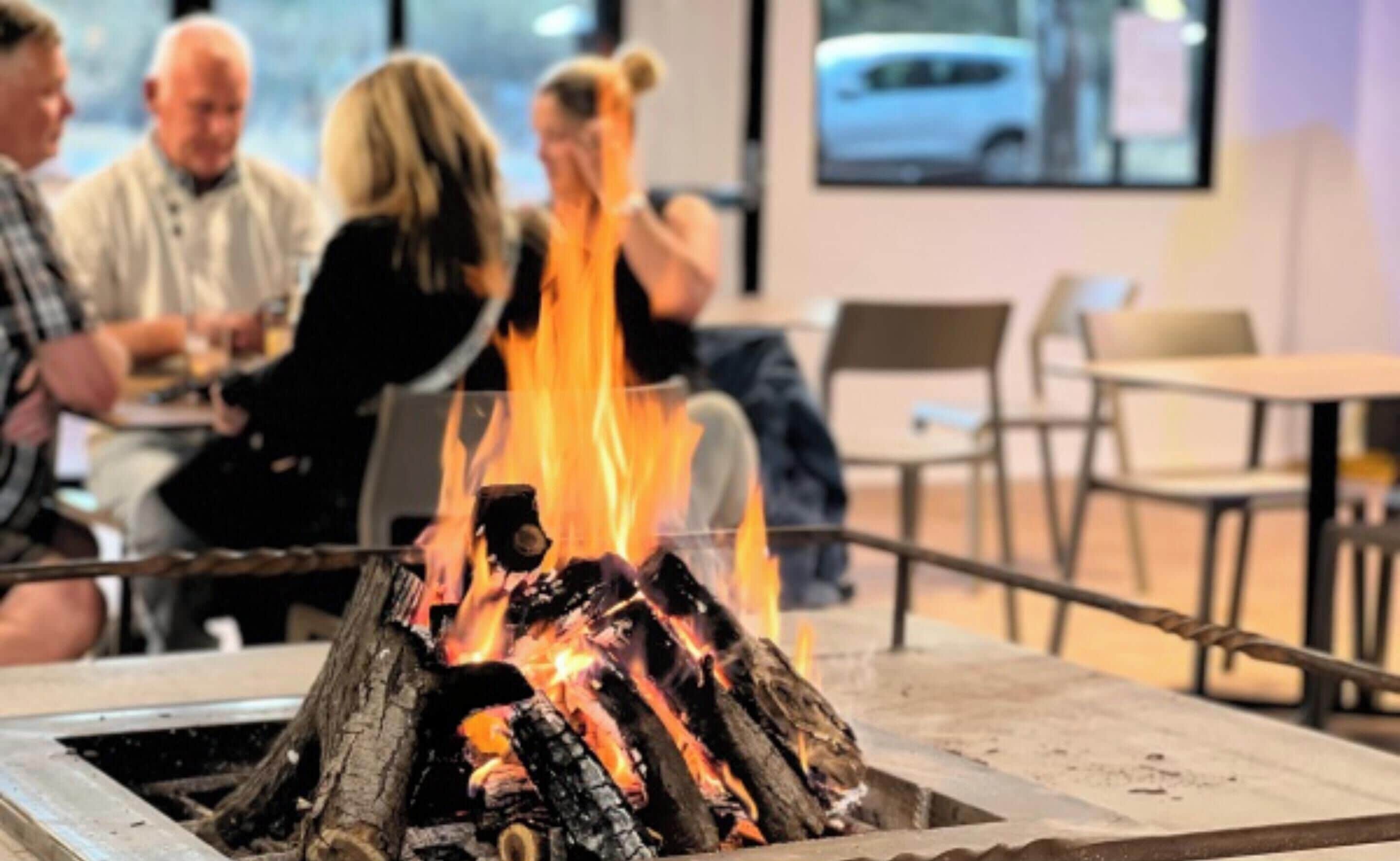 A group of people sitting around a fire pit in a modern indoor setting.