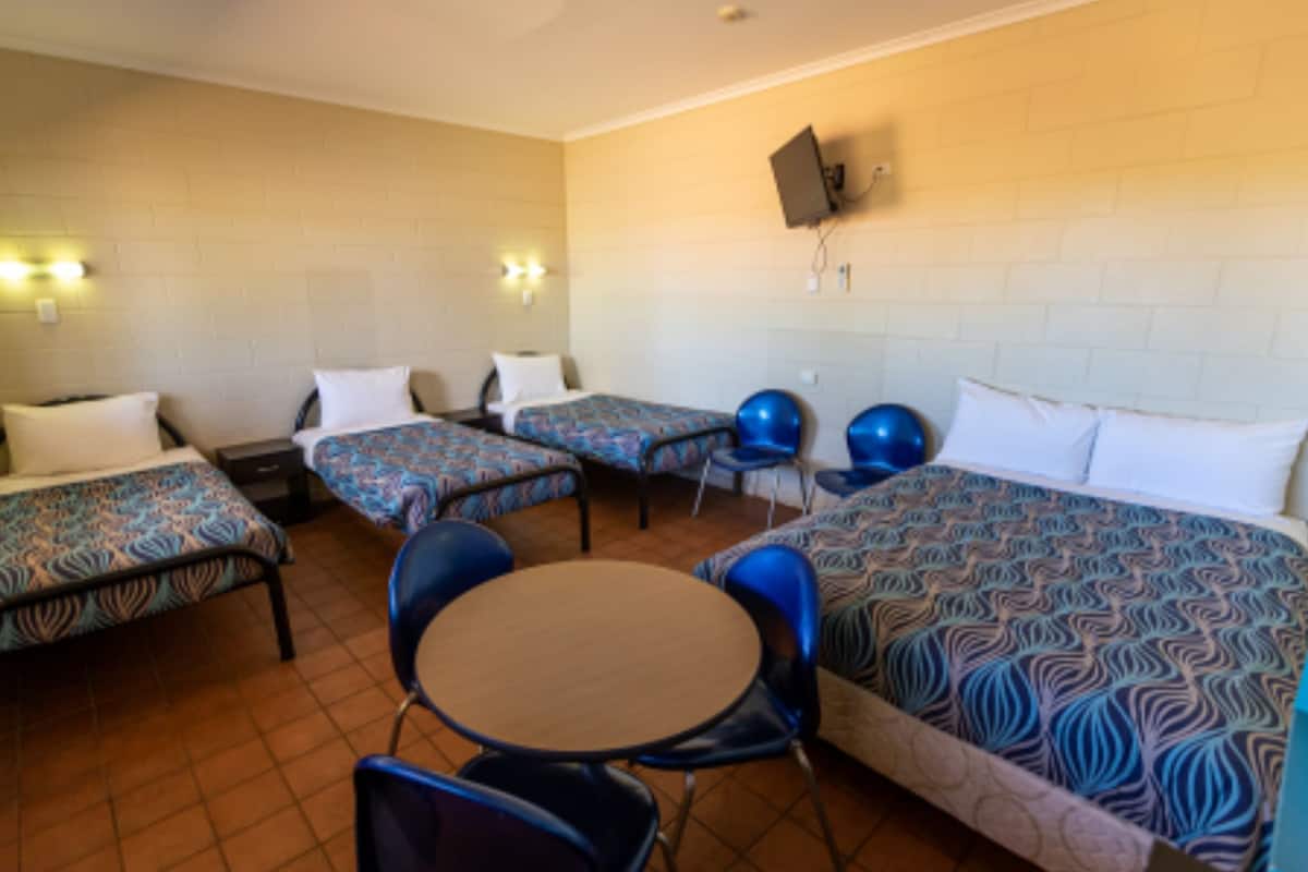 A motel room with four single beds, a round table, and two blue chairs.