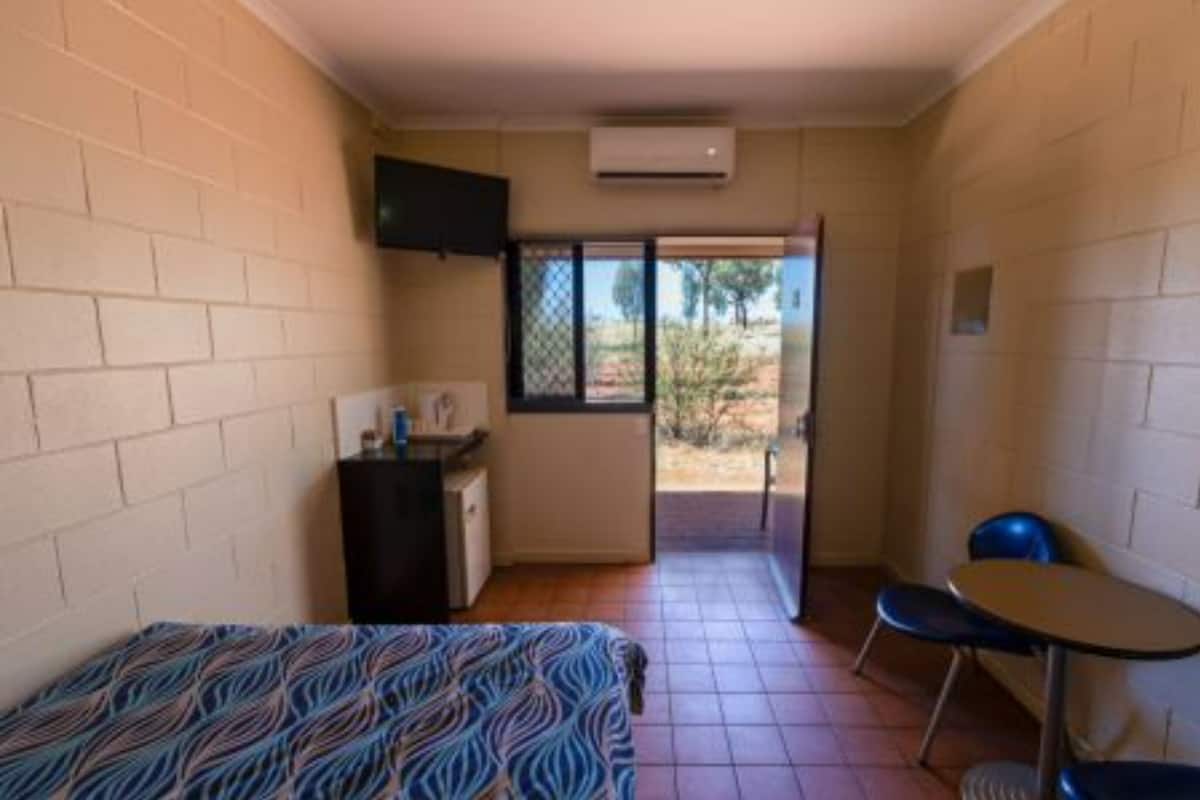 A small room with a bed, a desk, a chair, and a television. There is a window with a view of the outside.