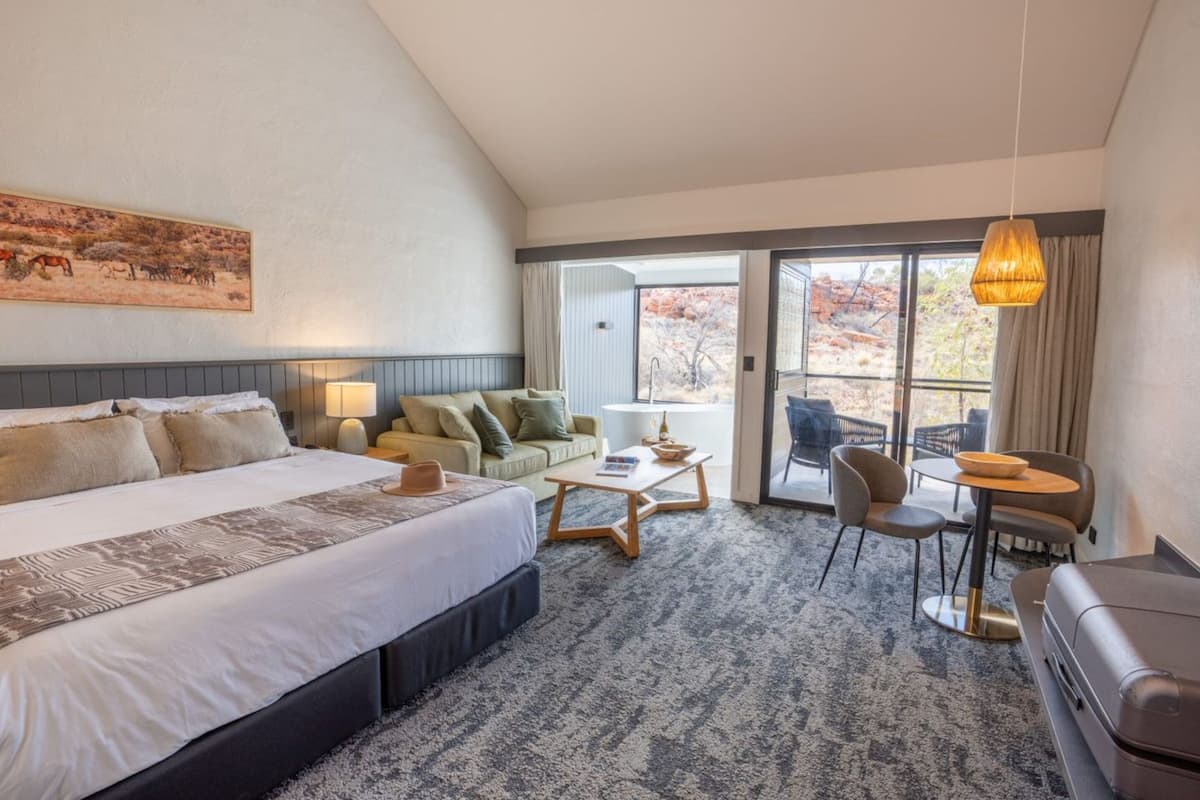 A hotel room with a large bed, a sofa, a coffee table, and a dining area with chairs and a table.