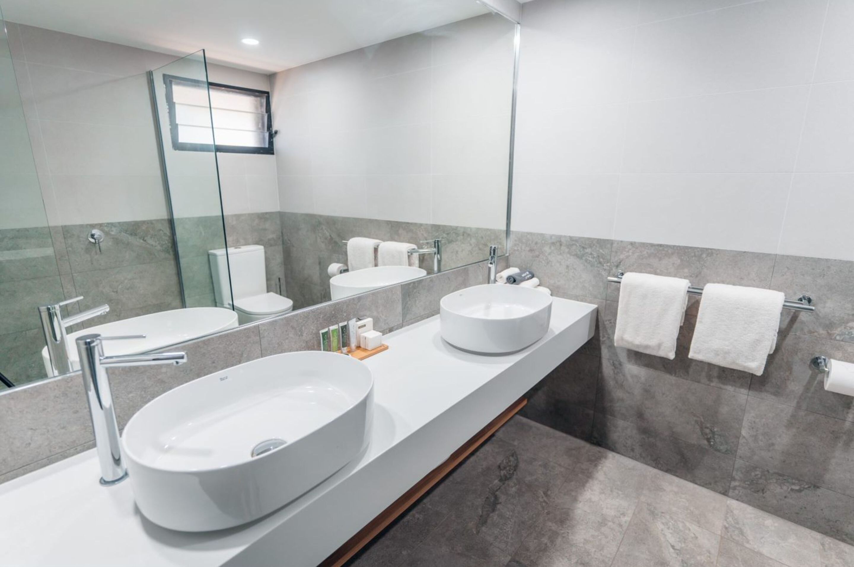 A modern bathroom with two sinks, a large mirror, and a toilet.