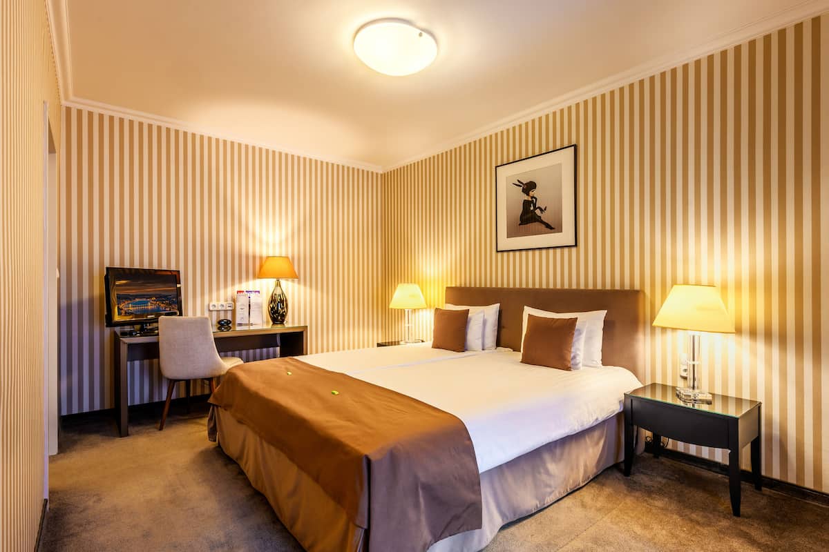 A hotel room with a large bed, two bedside lamps, a desk with a computer, and a chair.