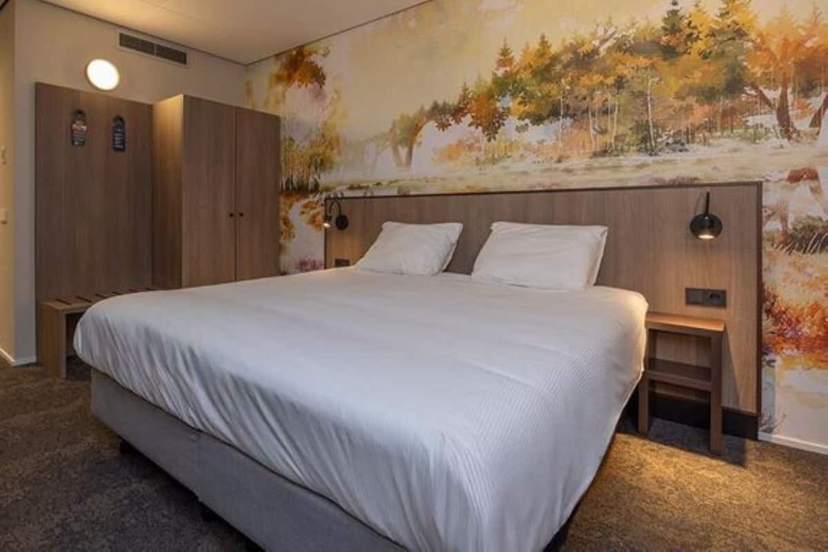 A bedroom with a large bed, wooden wardrobe, and a wall mural.