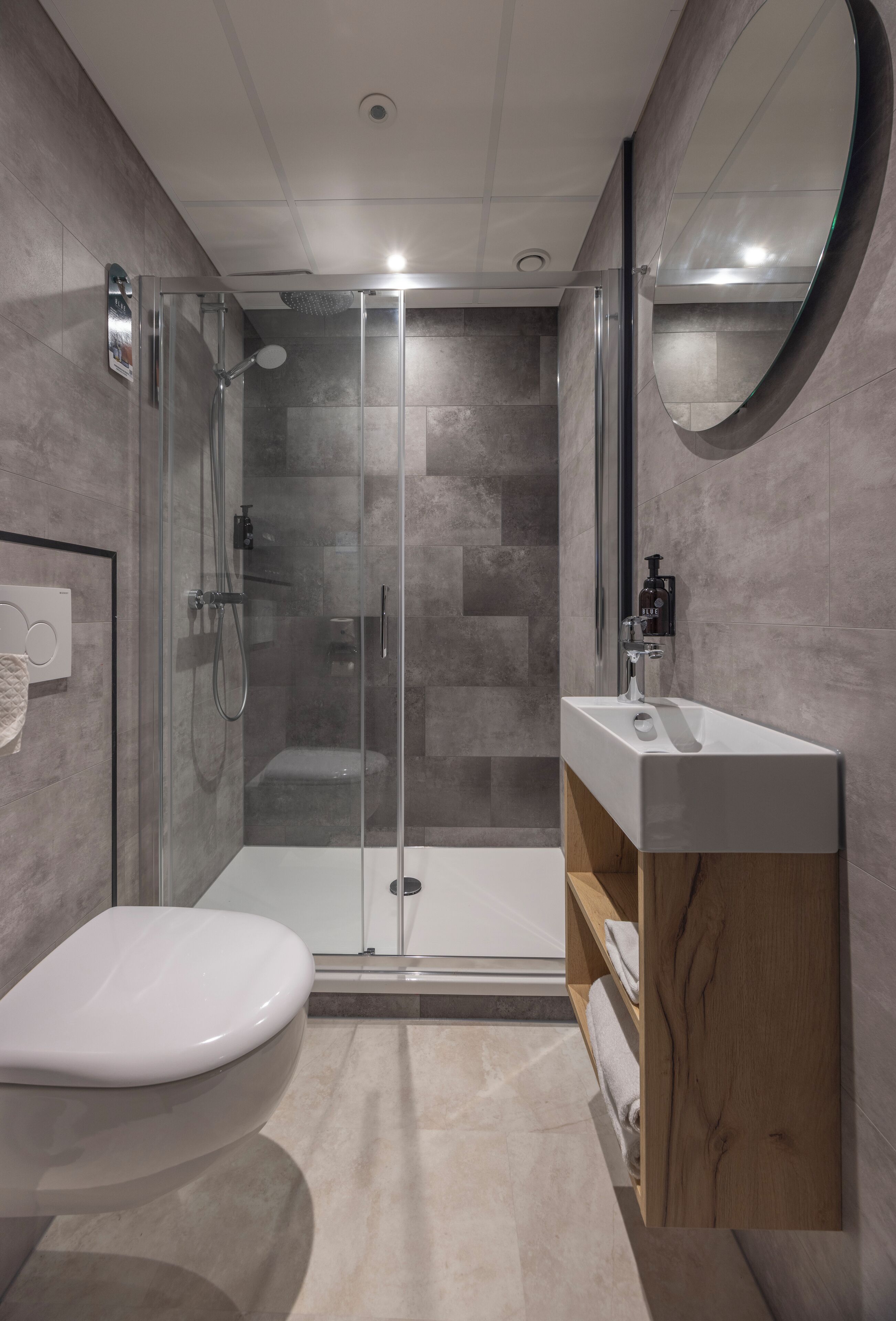 Ein modernes Badezimmer mit einer gläsernen Duschkabine, einer weißen Toilette und einem Holzwaschtisch.