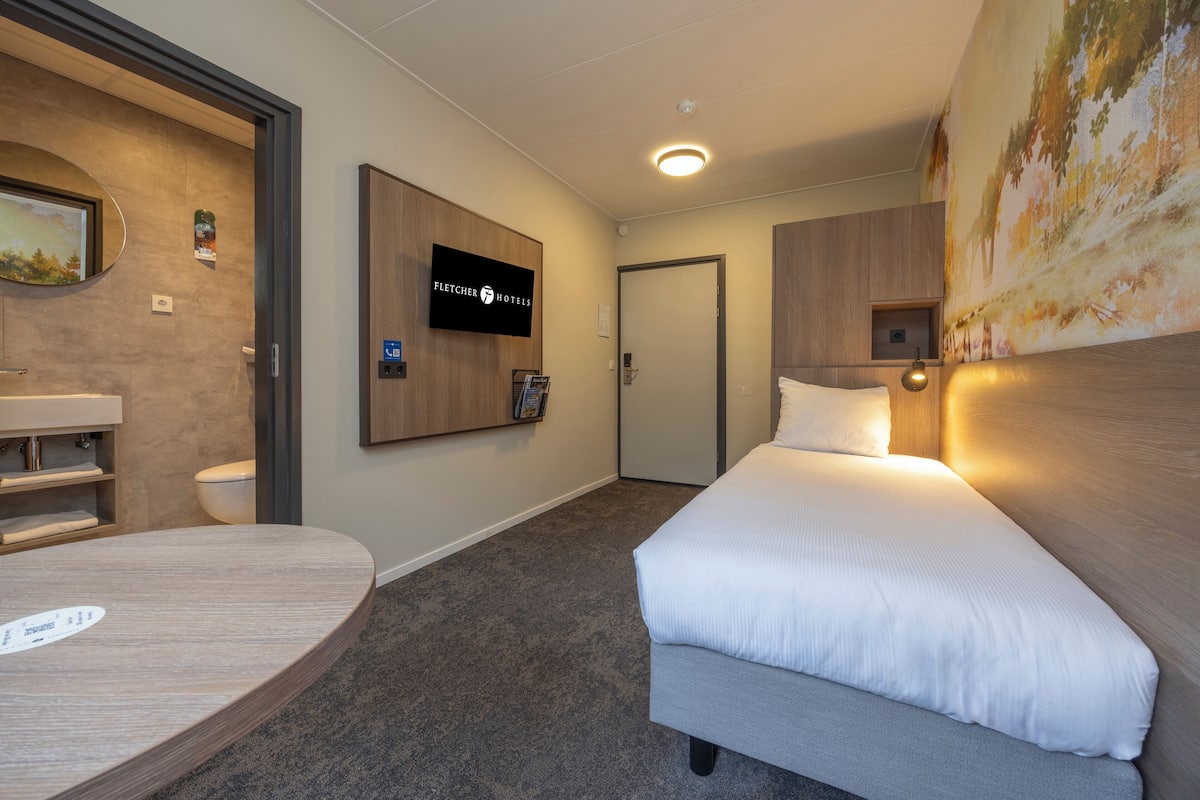 A hotel room with a bed, a round table, a television, and a painting on the wall.
