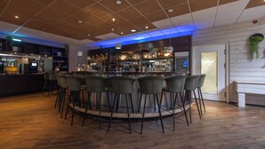 A bar area with a wooden floor, bar stools, and a counter with various bottles and glasses. - Fletcher Hotel-Restaurant Mooi Veluwe (Putten)