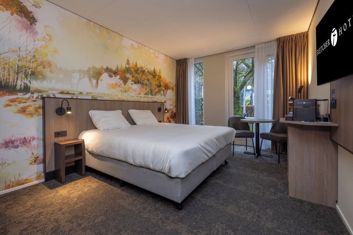 A hotel room with a large bed, a desk, and a TV.