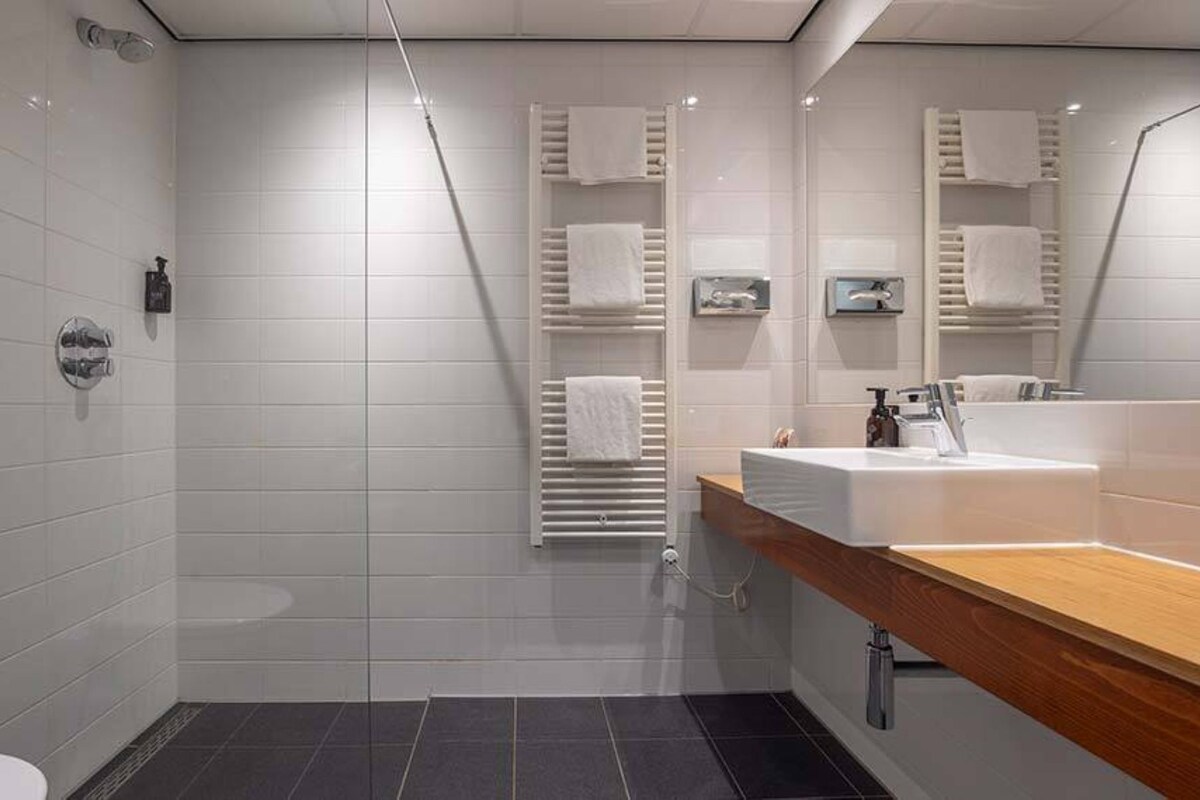 A modern bathroom with a shower, a toilet, a sink with a wooden countertop, and a towel rack with towels.