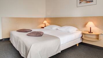 A neatly made bed with two pillows, a bedside table with a lamp, and a painting on the wall.