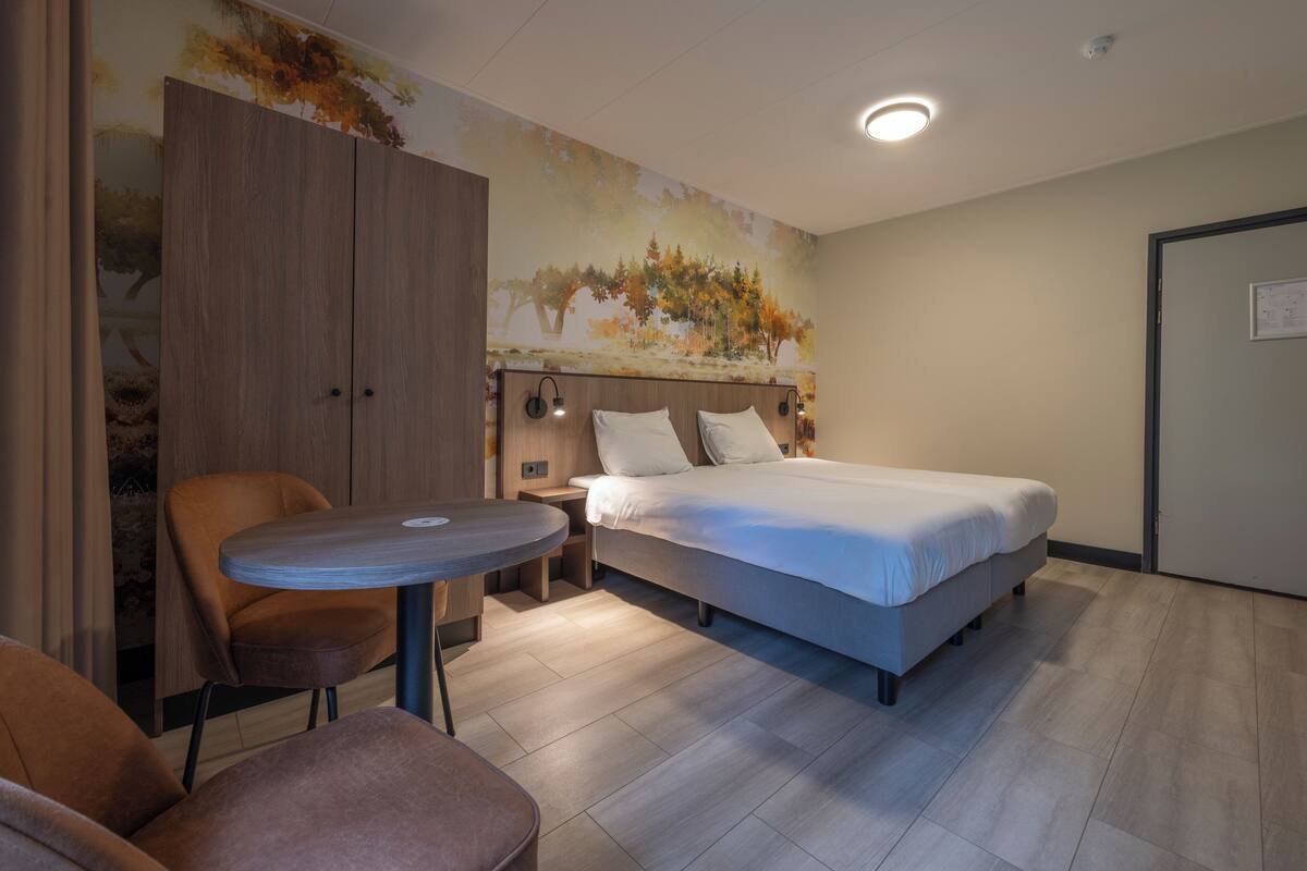 A hotel room with a bed, a round table, a chair, and a wardrobe.