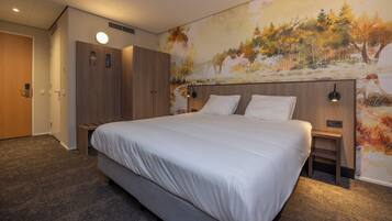 A modern hotel room with a large bed, wooden wardrobe, and a mural of autumn trees on the wall.