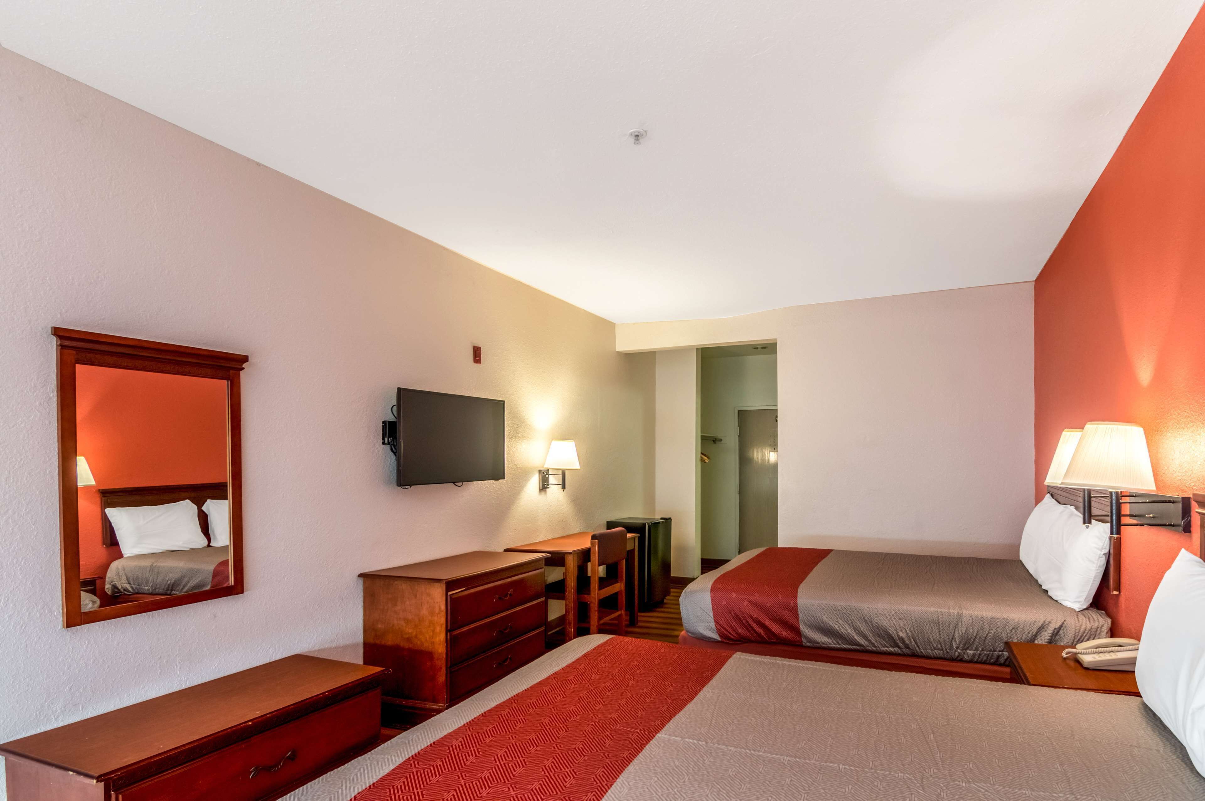 Ein Hotelzimmer mit zwei Betten, einem Fernseher, einem Schreibtisch mit Stuhl, einem Schminktisch und einem Spiegel.