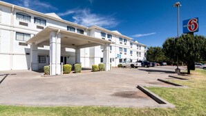 Un motel con entrada cubierta, estacionamiento y un letrero que indica el nombre del motel.