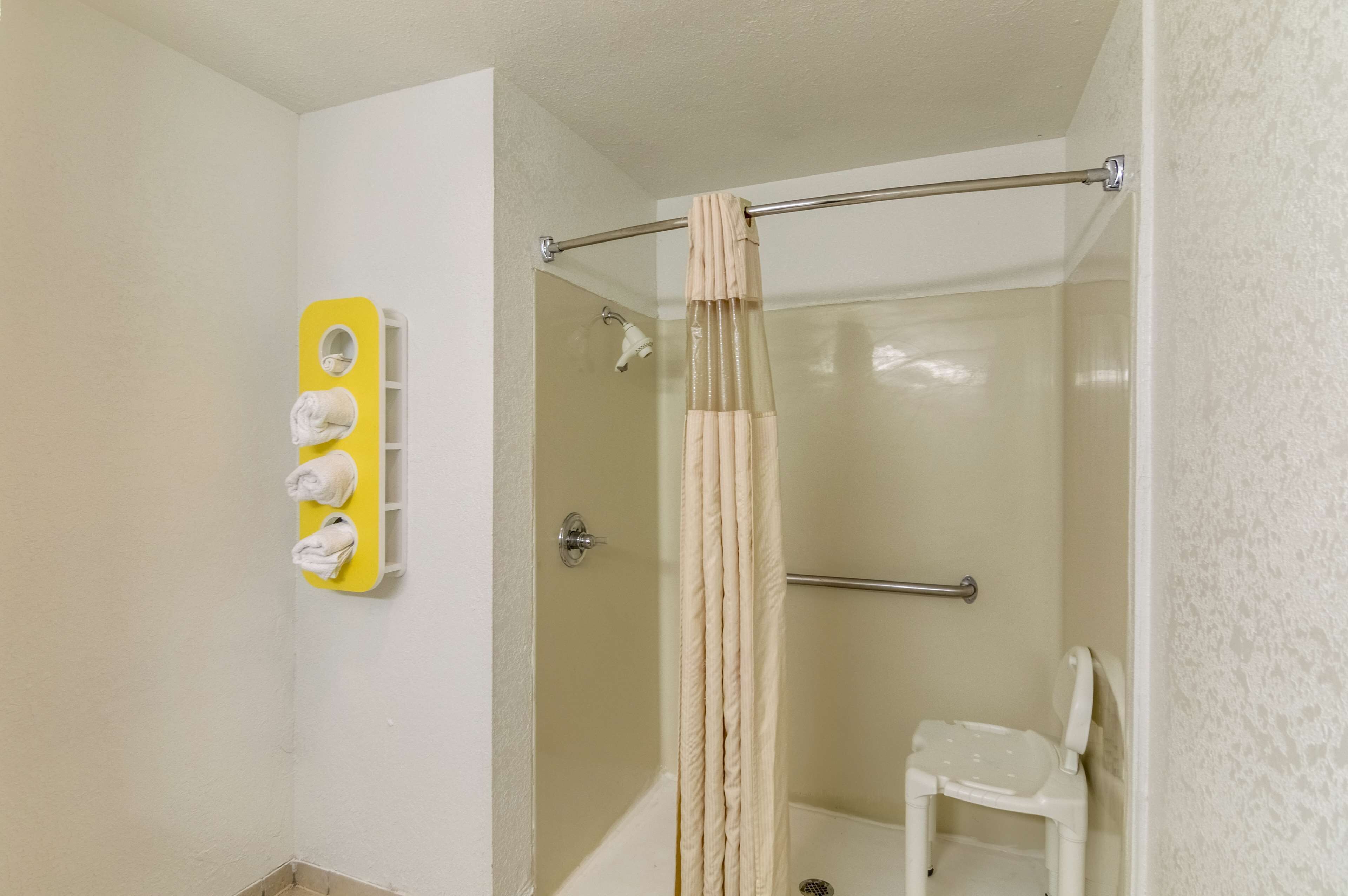 Een douche met een beige gordijn, een witte stoel en een gele handdoekhouder met handdoeken.