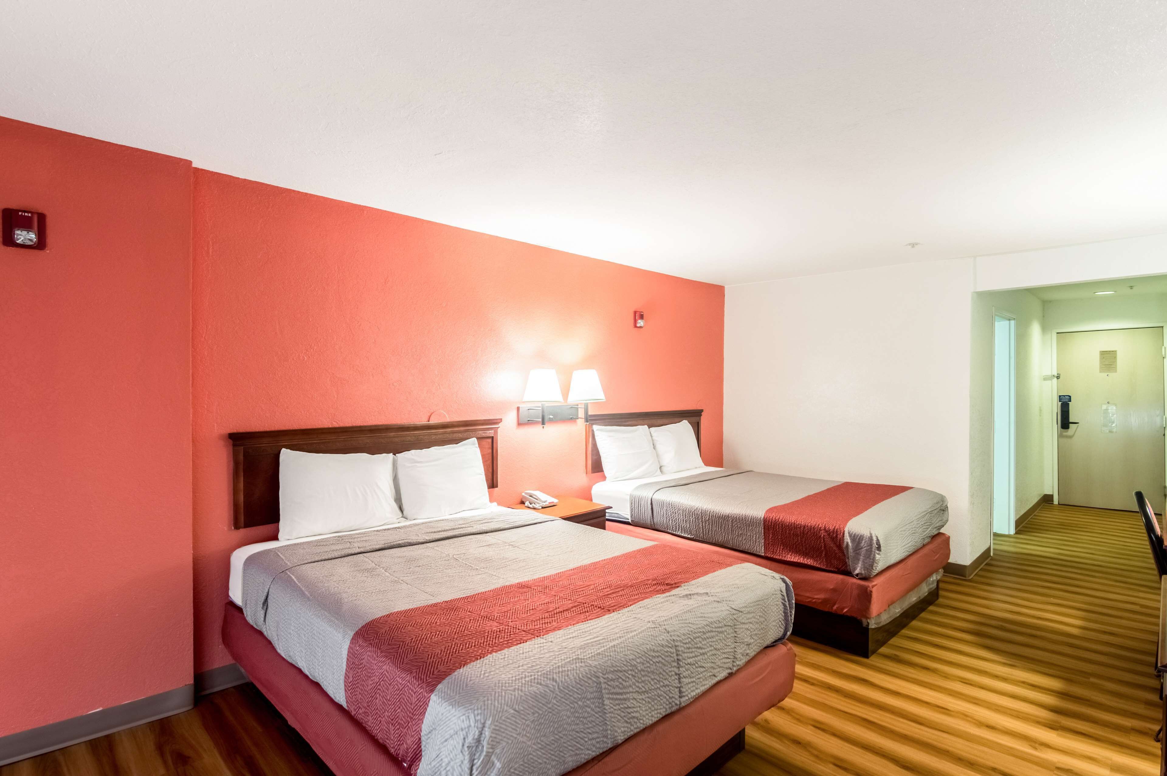 Habitación de hotel con dos camas, piso de madera y una pared de acento roja.