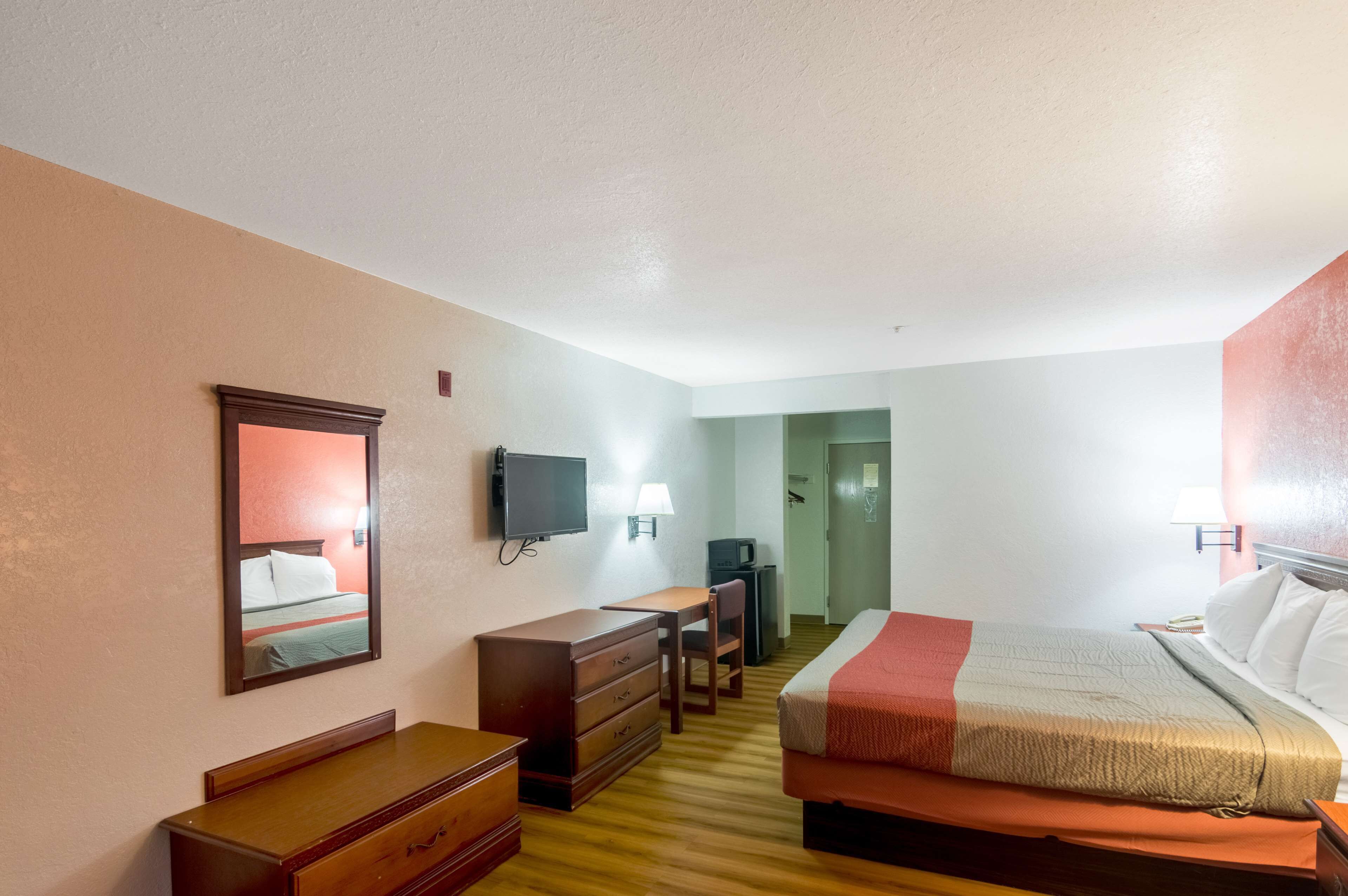 Une chambre d’hôtel comprenant un lit, une commode, un bureau, une télévision et un miroir.